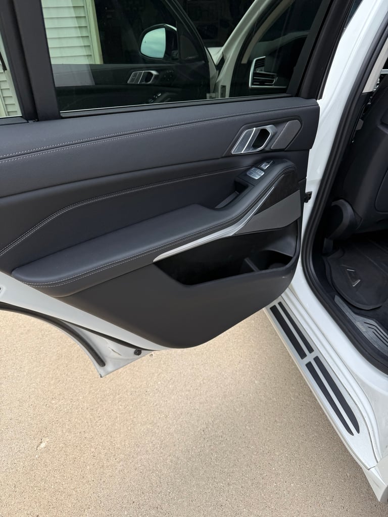 Open drivers side door of white vehicle showing gray interior panel with controls and window mechanisms