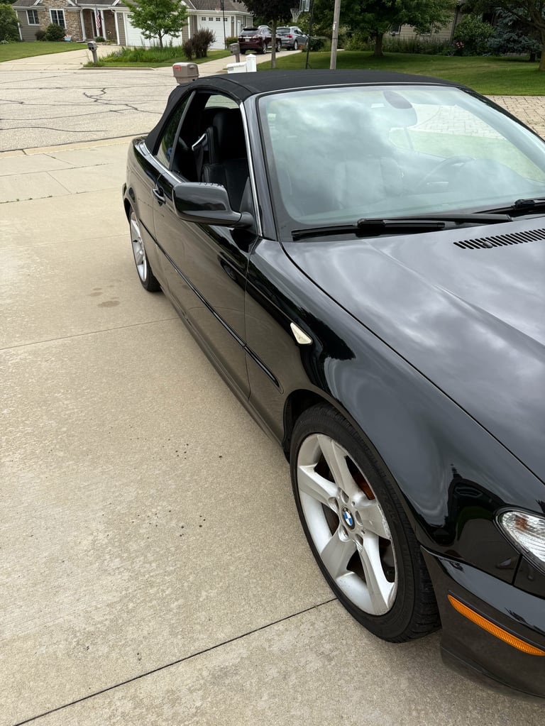 Black convertible car with top down parked in driveway of suburban home