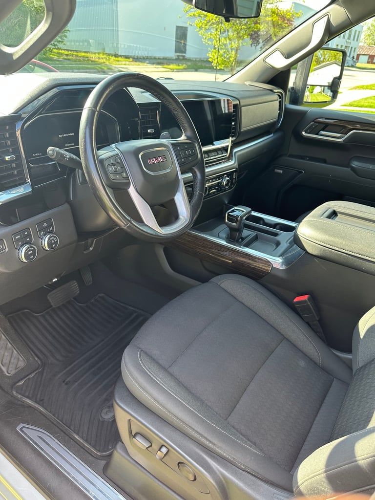 Interior view of GMC truck showing steering wheel, dashboard, black and tan upholstered seats, and center console with digital display