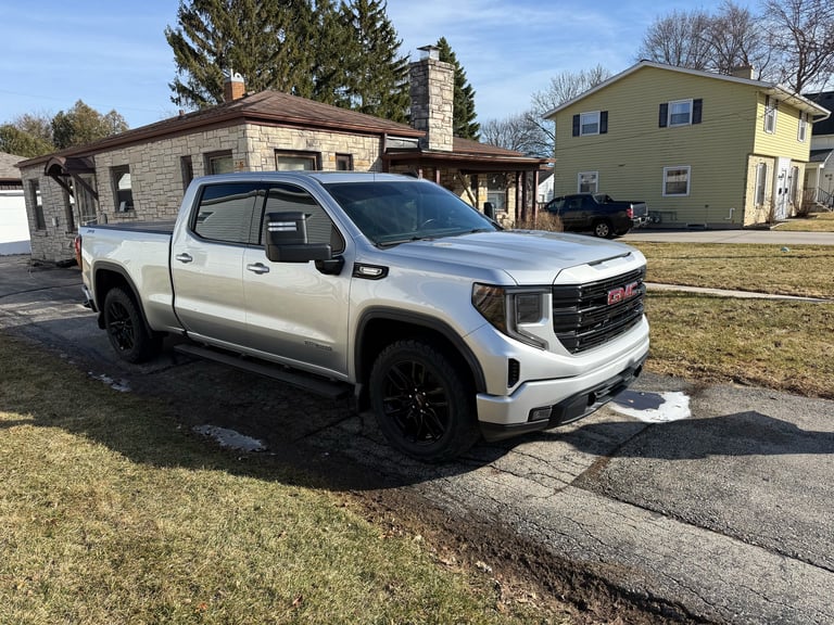 Silver GMC Sierra pickup truck parked in residential driveway with house in background